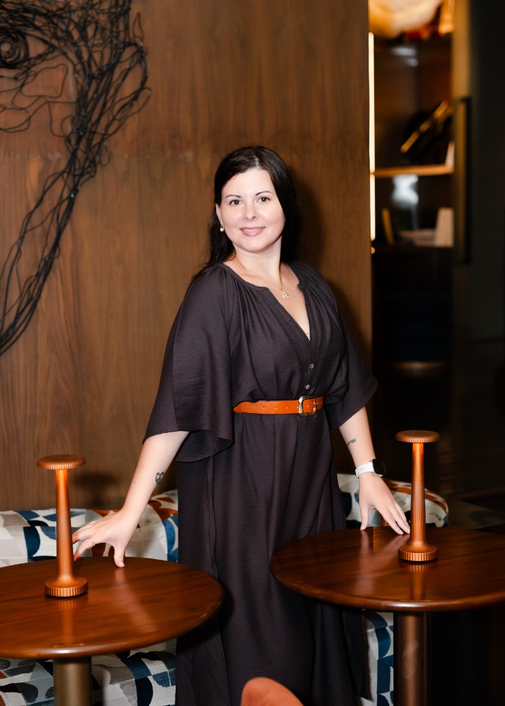 Yuli Varzar standing in a lounge, smiling between two pedestal tables